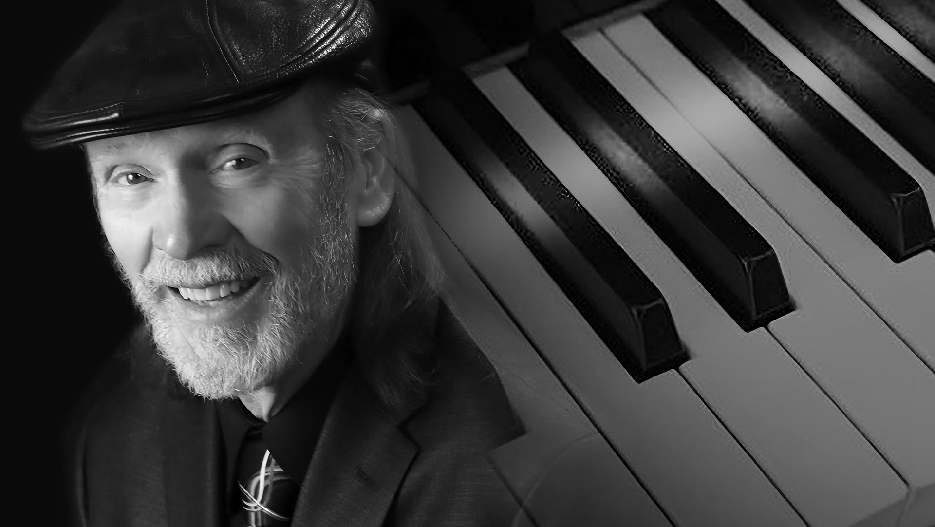 Bob Duquesne in a black leather flat cap, smiling over the keys of a grand piano.